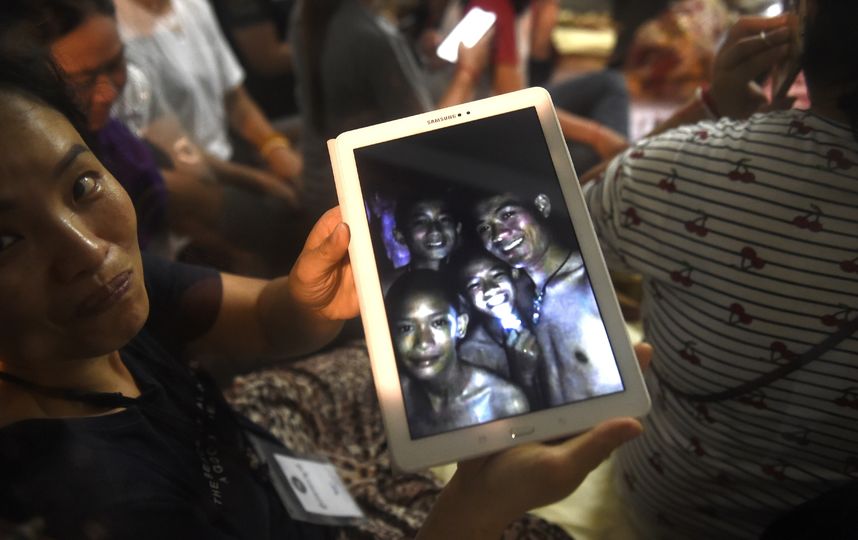Родственники пропавших детей показывают на планшете их снимки, которые сделали спасатели в пещере. Дети живы. Фото AFP
