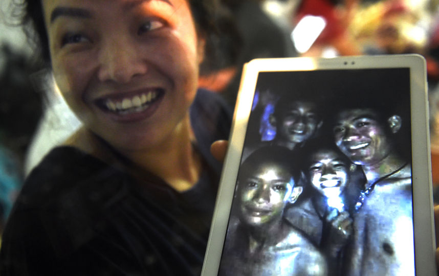 Родственники пропавших детей показывают на планшете их снимки, которые сделали спасатели в пещере. Дети живы. Фото AFP