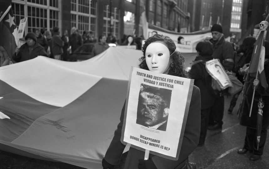 Женщина в маске держит плакат с фото мужчины, похищенного во времена диктатуры Пиночета в Чили. Фото Getty