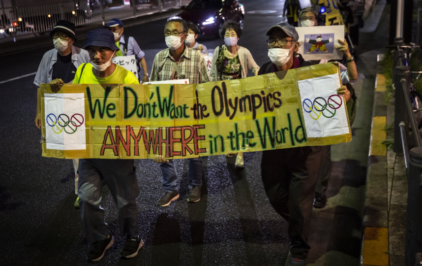 Работники ресторана в квартале Кабуки-тё в Токио после закрытия своего заведения 14 июля 2021 года. Надпись на плакате гласит: "Мы не хотим Олимпиаду нигде в мире". Фото Getty