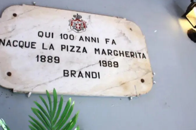 Эту табличку повесили на стене ресторана к столетию создания "Маргариты". Вообще, эта пицца символизирует флаг Италии: томаты отвечают за красный цвет, моцарелла – за белый, базилик – за зелёный. Фото Соцсети.
